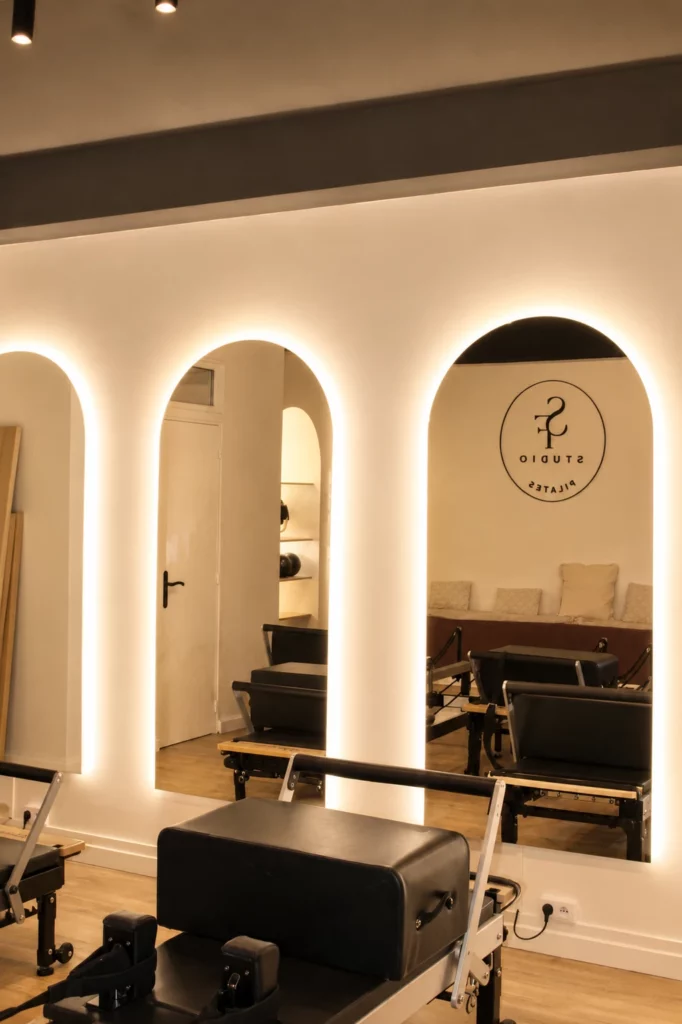 Studio équipé de machines Pilates Reformer face à des miroirs en arche rétroéclairés.